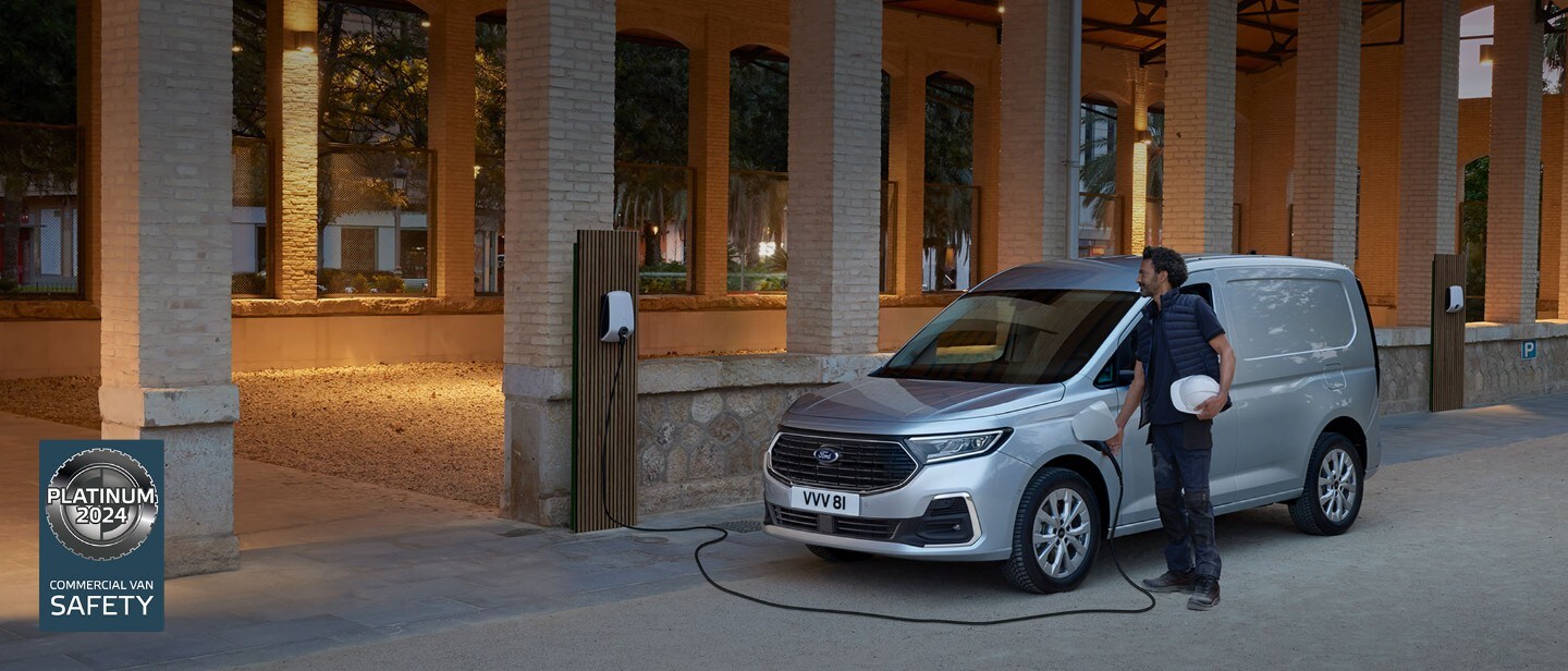 Ein Mann mit Schutzhelm steckt ein Wallbox-Ladekabel in einen Ford Transit Connect in Stardust Silver.