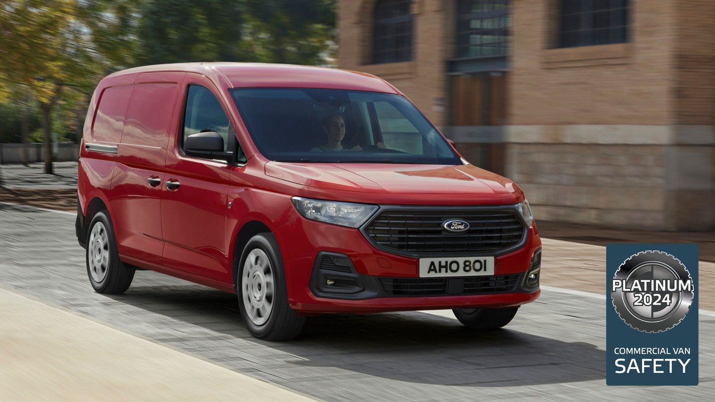 Ford Transit Connect Trend in Maple Red mit Kühlergrill und automatischen Scheinwerfern fährt eine Strasse entlang.