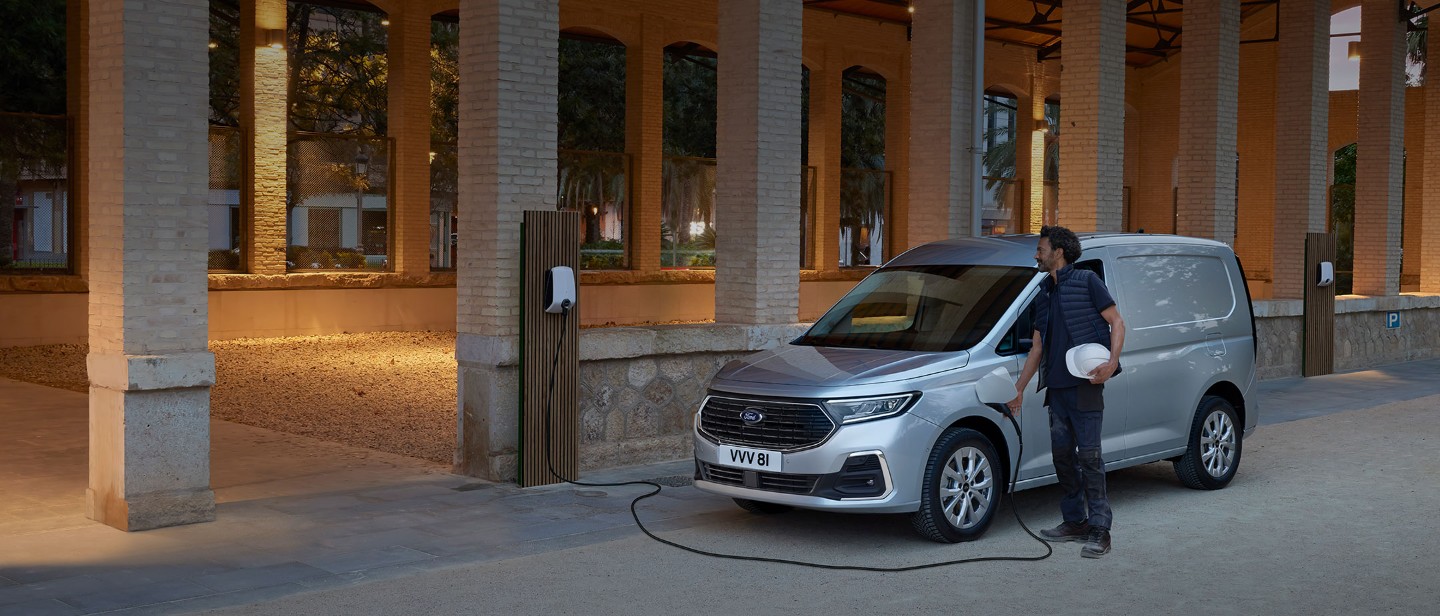 Ein Mann mit Schutzhelm steckt ein Wallbox-Ladekabel in einen Ford Transit Connect in Stardust Silver.