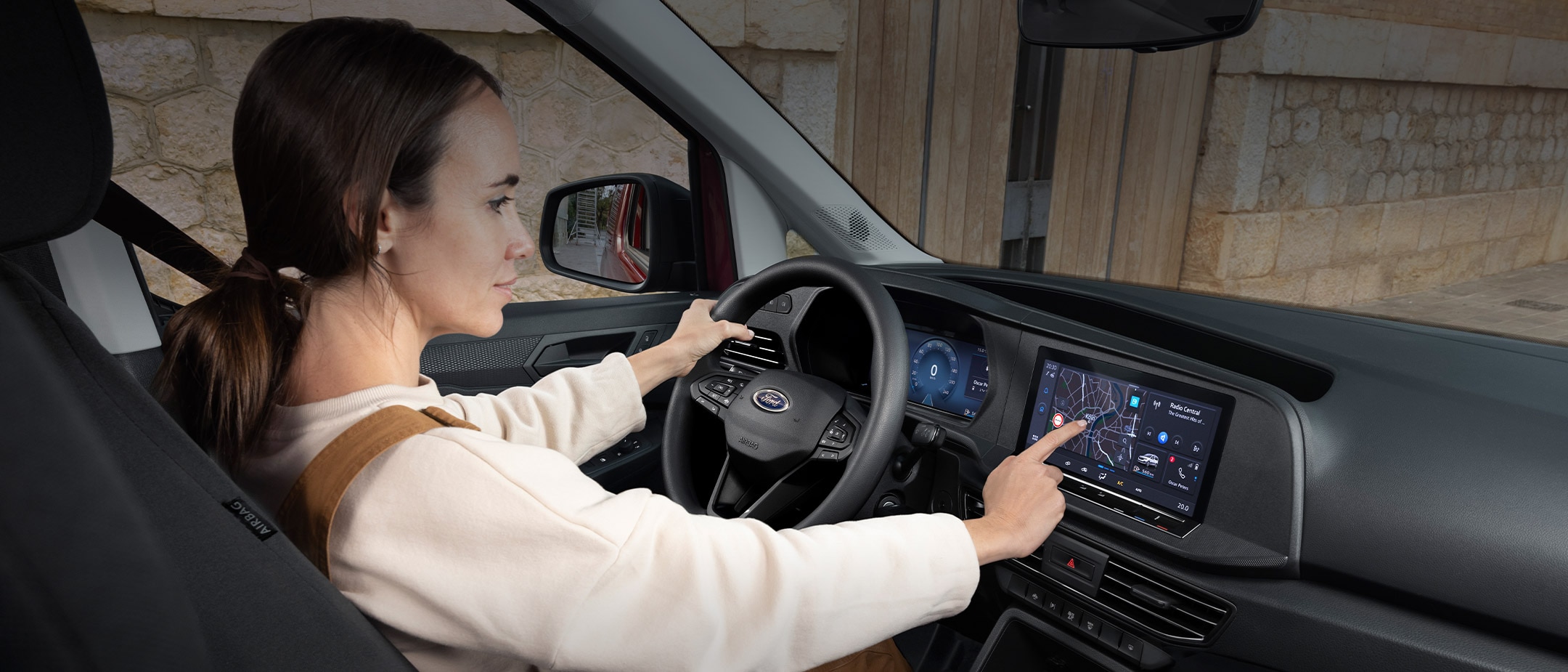 Eine Frau berührt den 10-Zoll-Touchscreen, während sie auf dem Fahrersitz des Ford Transit Connect sitzt.