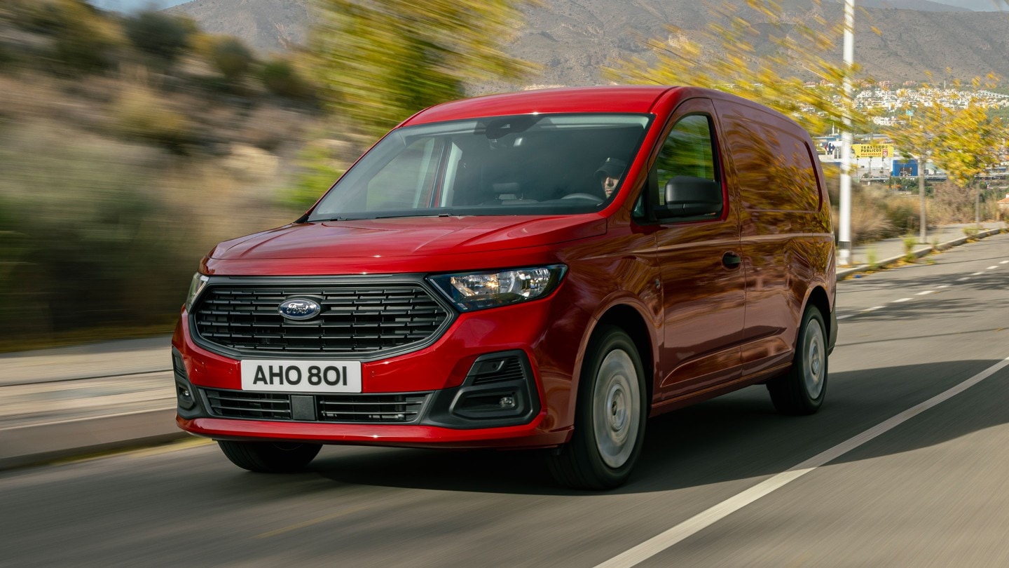 Ford Transit Connect in Maple Red mit Kühlergrill und Scheinwerfern fährt eine Strasse entlang.