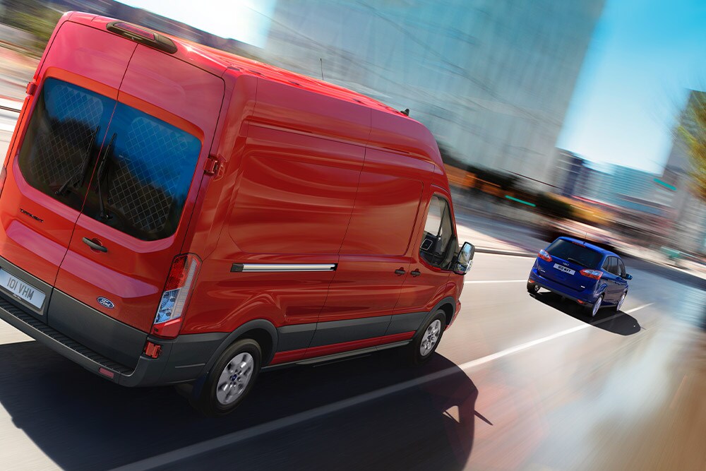 Roter Ford Transit Kastenwagen fährt auf einer Strasse.