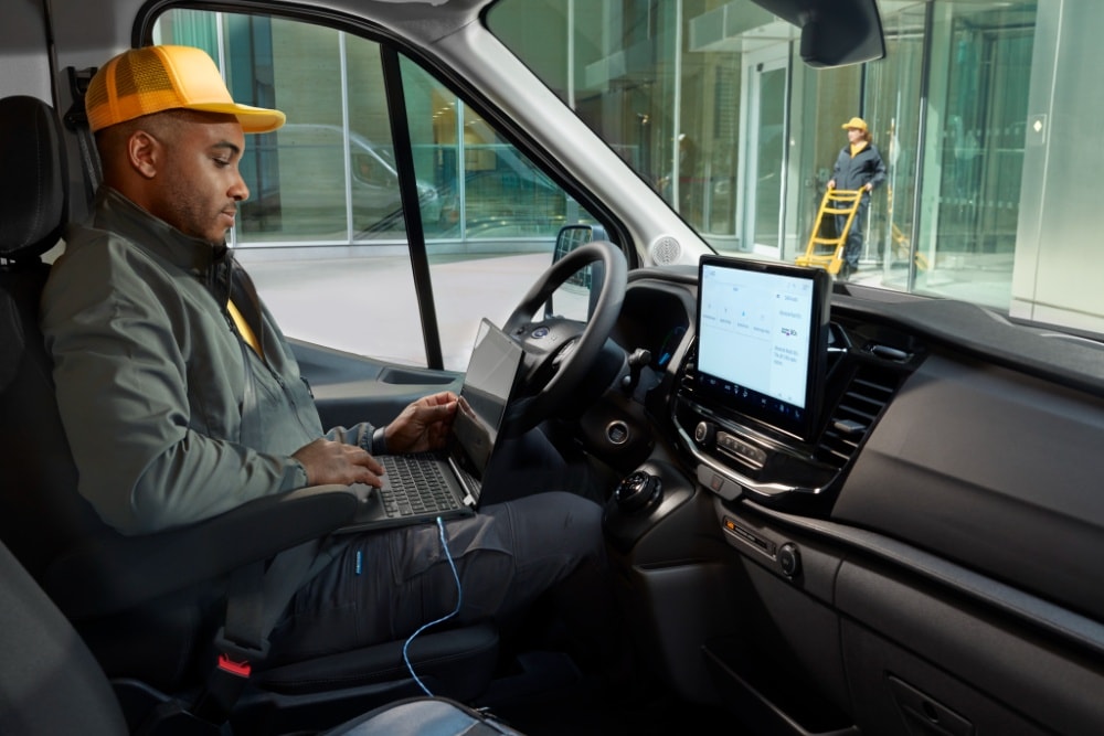 Ein Mann, der auf dem Fahrersitz eines Ford Transit sitzt und einen Laptop benutzt.