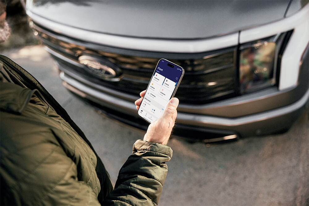 Ein Mann, der vor einem Ford Ranger auf sein Smartphone schaut.