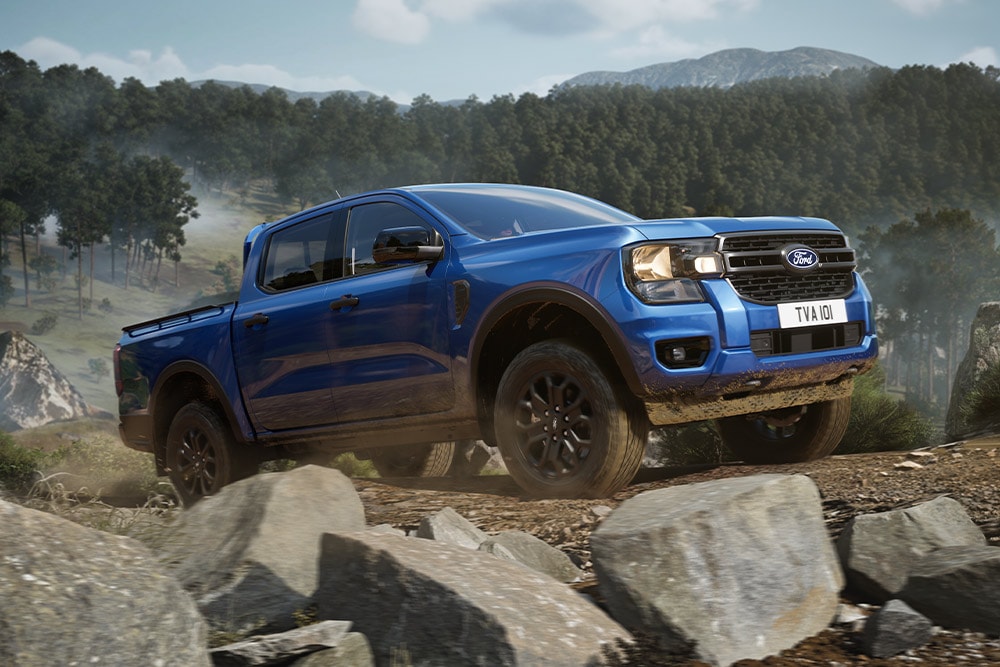 Ein blauer Ford Ranger Pick-up fährt auf einer unbefestigten Strasse durch einen Wald und hinterlässt eine Staubwolke.