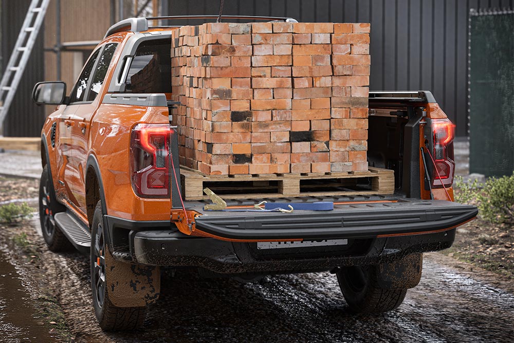 Blick auf die Rückseite eines orangefarbenen Ford Ranger, dessen Ladefläche mit einem Palett Ziegelsteinen beladen ist.