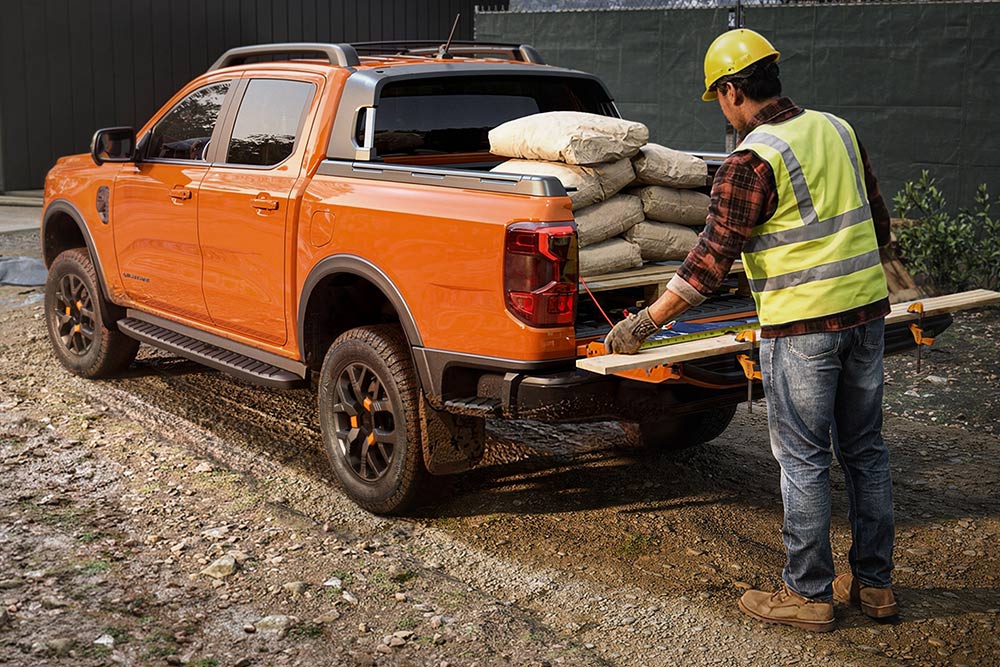 Ein Bauarbeiter, der Zementsäcke auf die Ladefläche eines orangefarbenen Ford Ranger lädt.