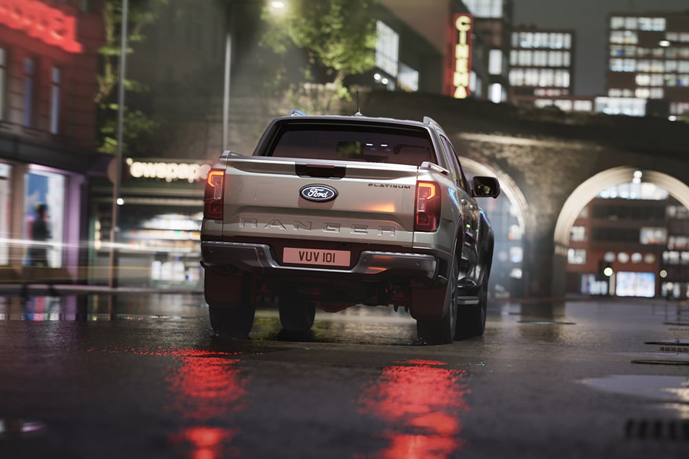 Rückansicht eines silbernen Ford Ranger, der nachts durch eine neonbeleuchtete Stadtlandschaft fährt.