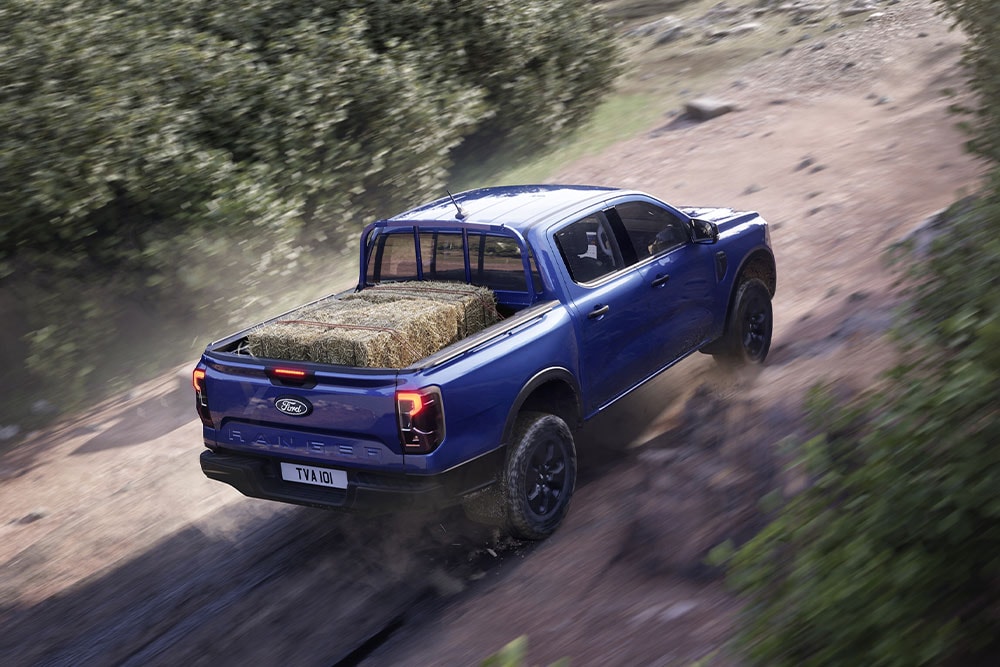 Blick von schräg oben auf einen beladenen blauen Ford Ranger, der auf einer Feldstrasse fährt.