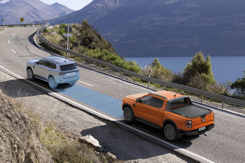 Ein orangefarbener Ford Ranger nutzt sein fortschrittliches Fahrassistenzsystem auf einer Küstenstrasse.