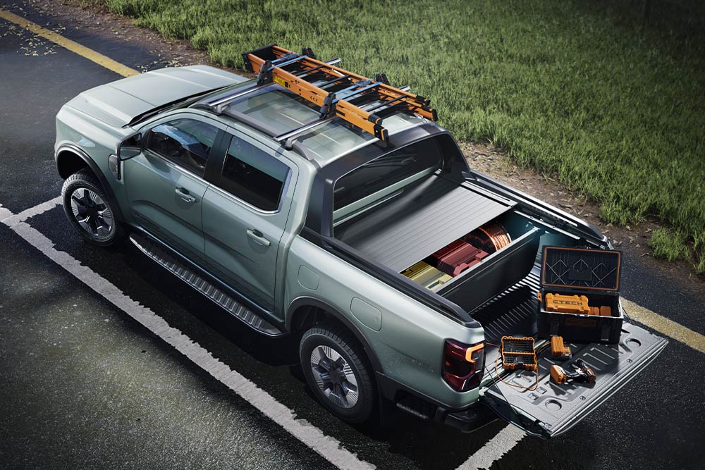 Rückansicht eines grauen Ford Ranger Pick-ups von oben, mit offener Ladefläche, Werkzeugen und Dachträger auf gepflastertem Untergrund.