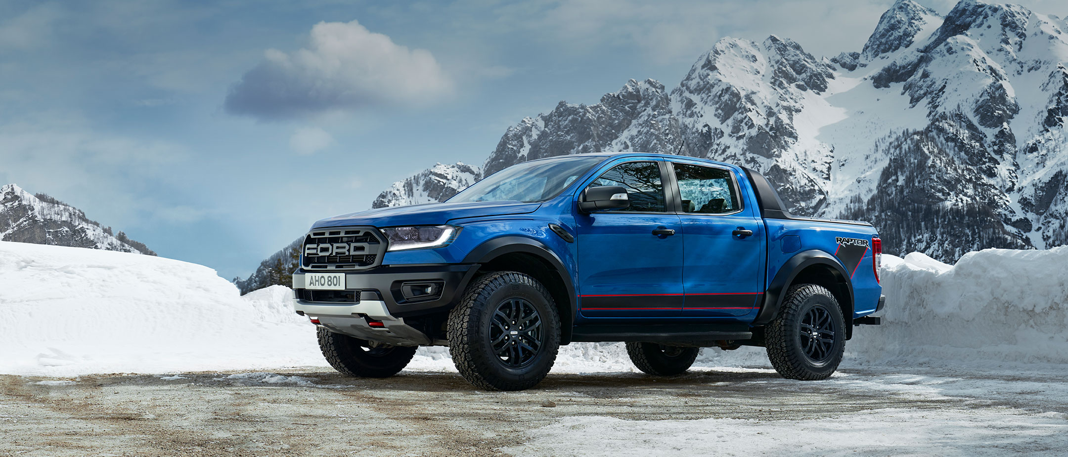 Blue Ford Ranger Raptor driving through a countryside, front three quarter view