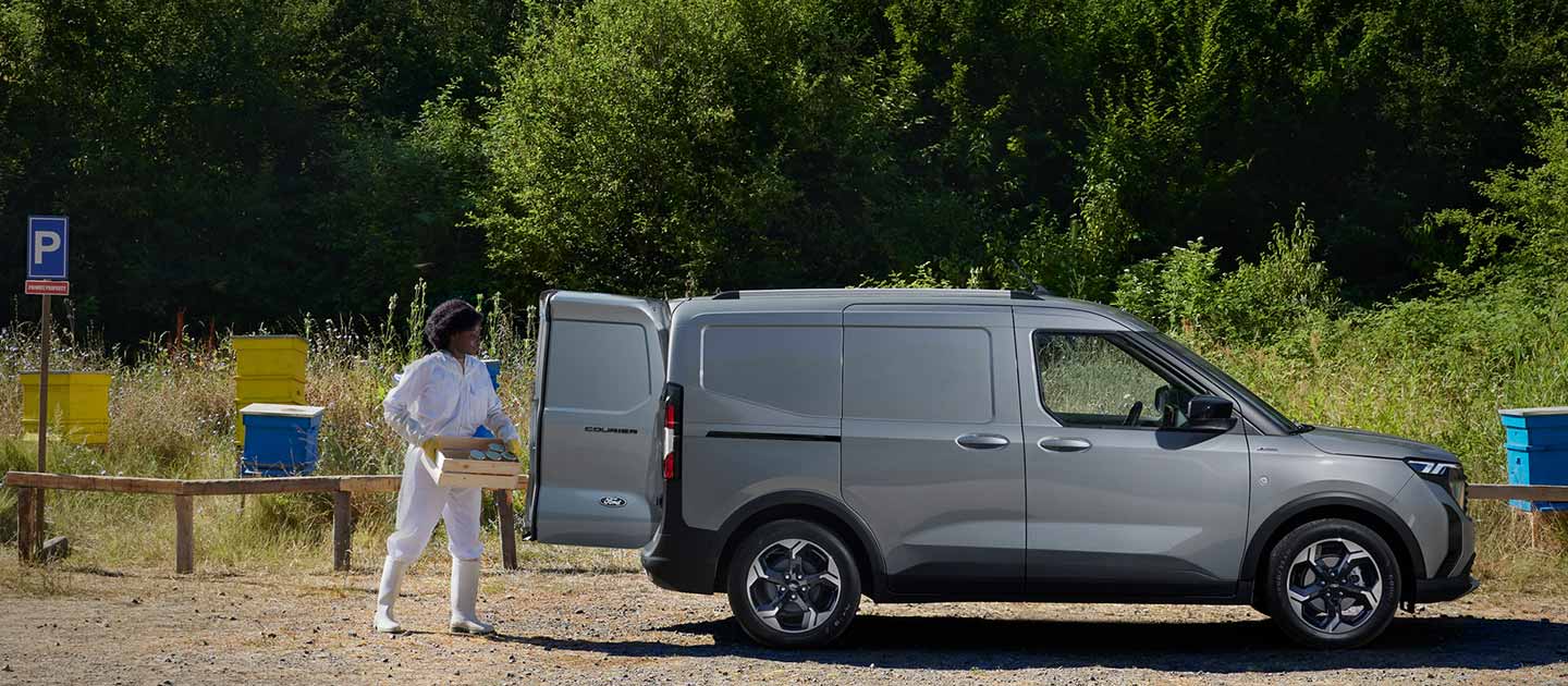 Ford E-Transit Courier in Grau – Seitenansicht, Frau belädt das Auto