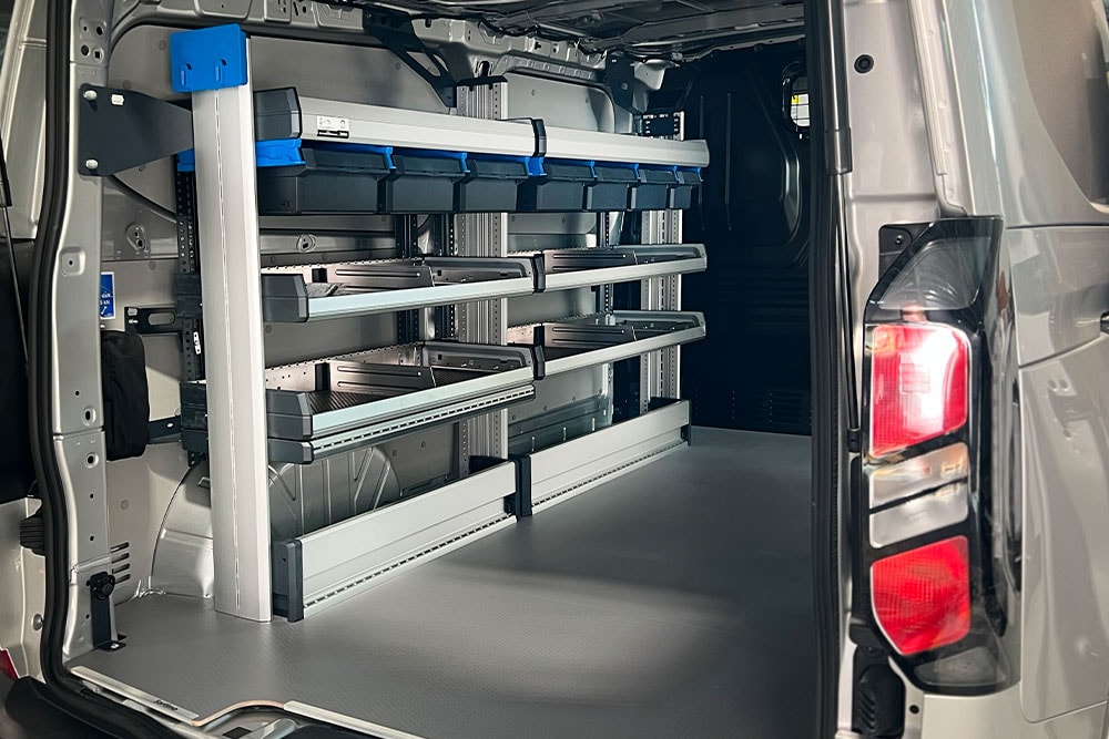 Hinterer Innenraum eines Ford Transit Transporters, der ein modulares Regalsystem mit verschiedenen Aufbewahrungsbehältern zeigt.