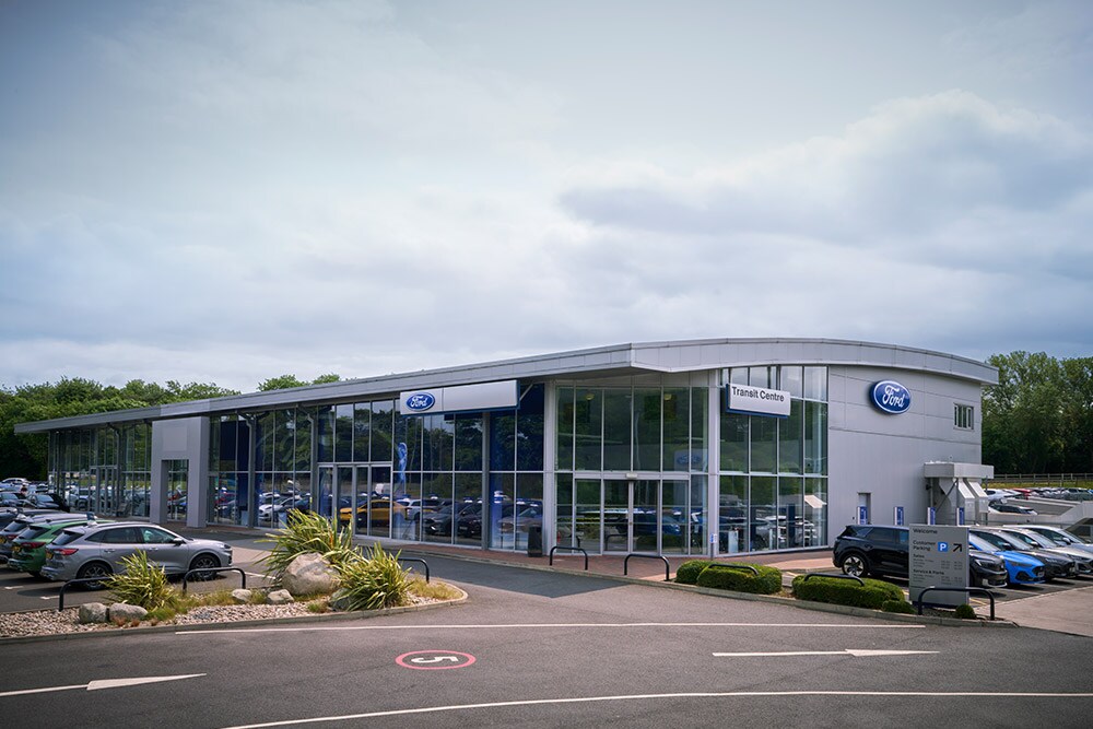 Aussenansicht eines modernen Ford-Autohauses mit verschiedenen Ford-Fahrzeugen davor.