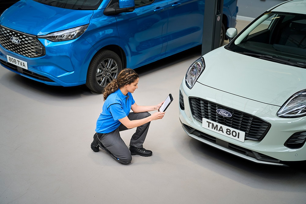 Ein Techniker kniet zwischen einem blauen Ford-Transporter und einem weissen Ford Puma und schaut auf ein Tablet.