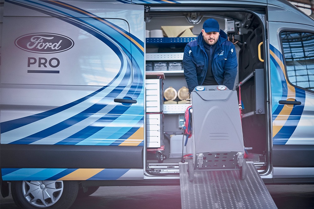 Ein mobiler Ford Pro Techniker holt Werkzeuge aus einem Transit-Transporter vor einem Geschäft.