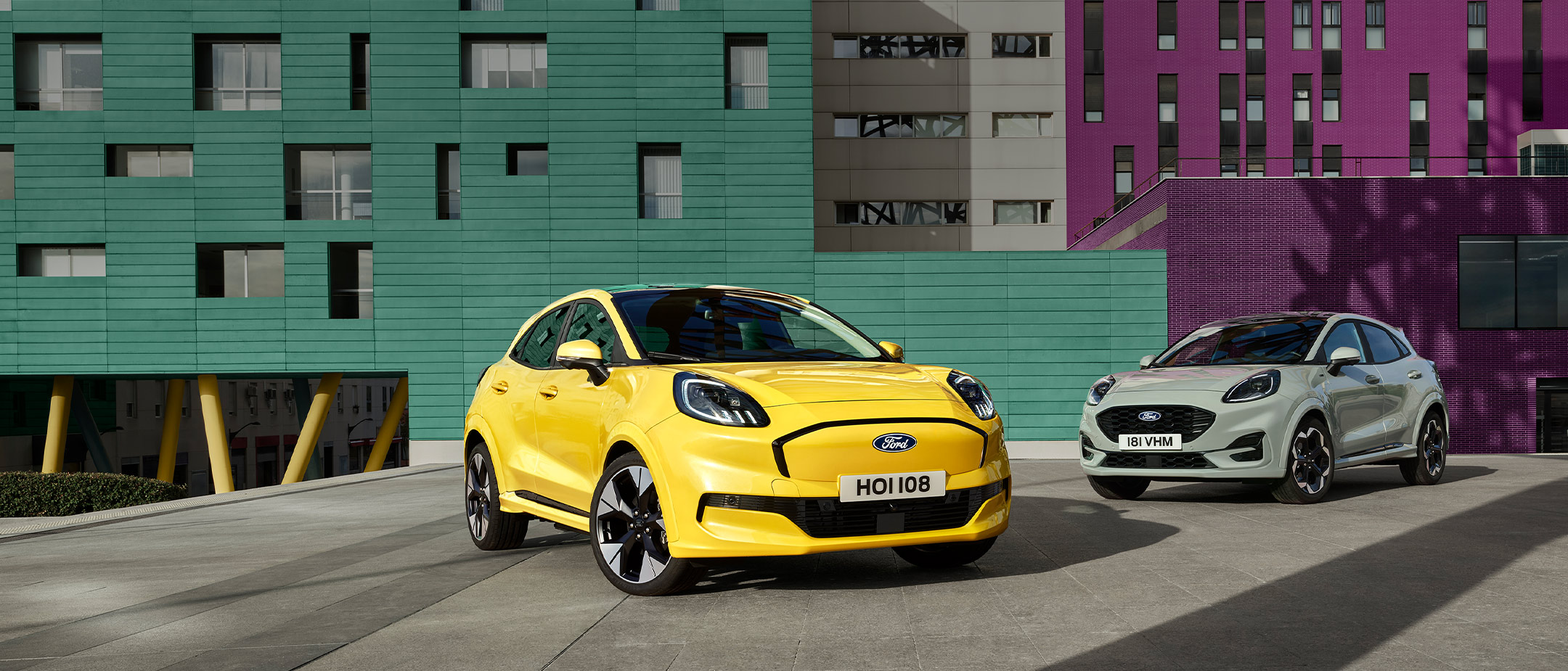 Ein vollelektrischer Ford Puma Gen-E® in Gelb ist neben einem grauen Ford Puma® mit EcoBoost®-Benzinmotor parkiert. 