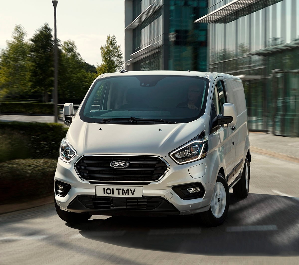 Ford Transit Custom in Silber fahren vor einem Gebäude mit Glasfront