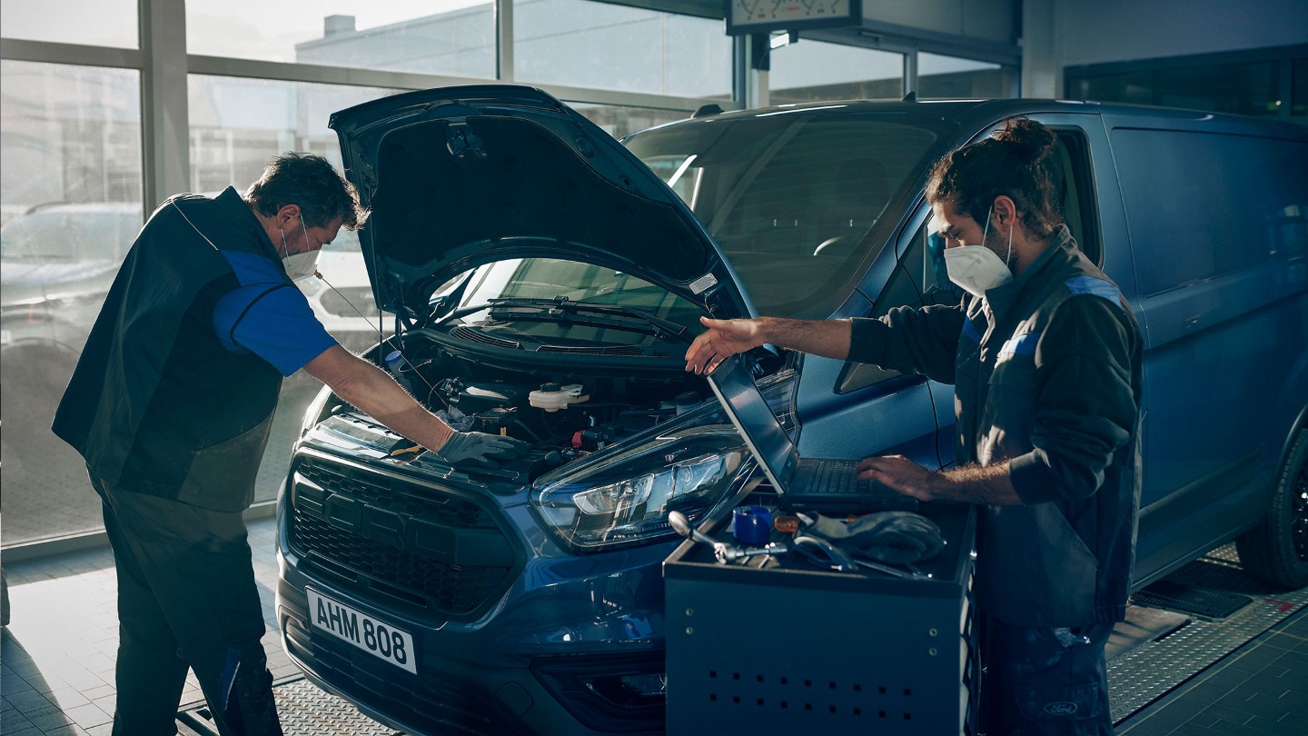 Zwei Mechaniker bei der Inspektion eines Ford Transit Custom in Blau mit geöffneter Motorhaube