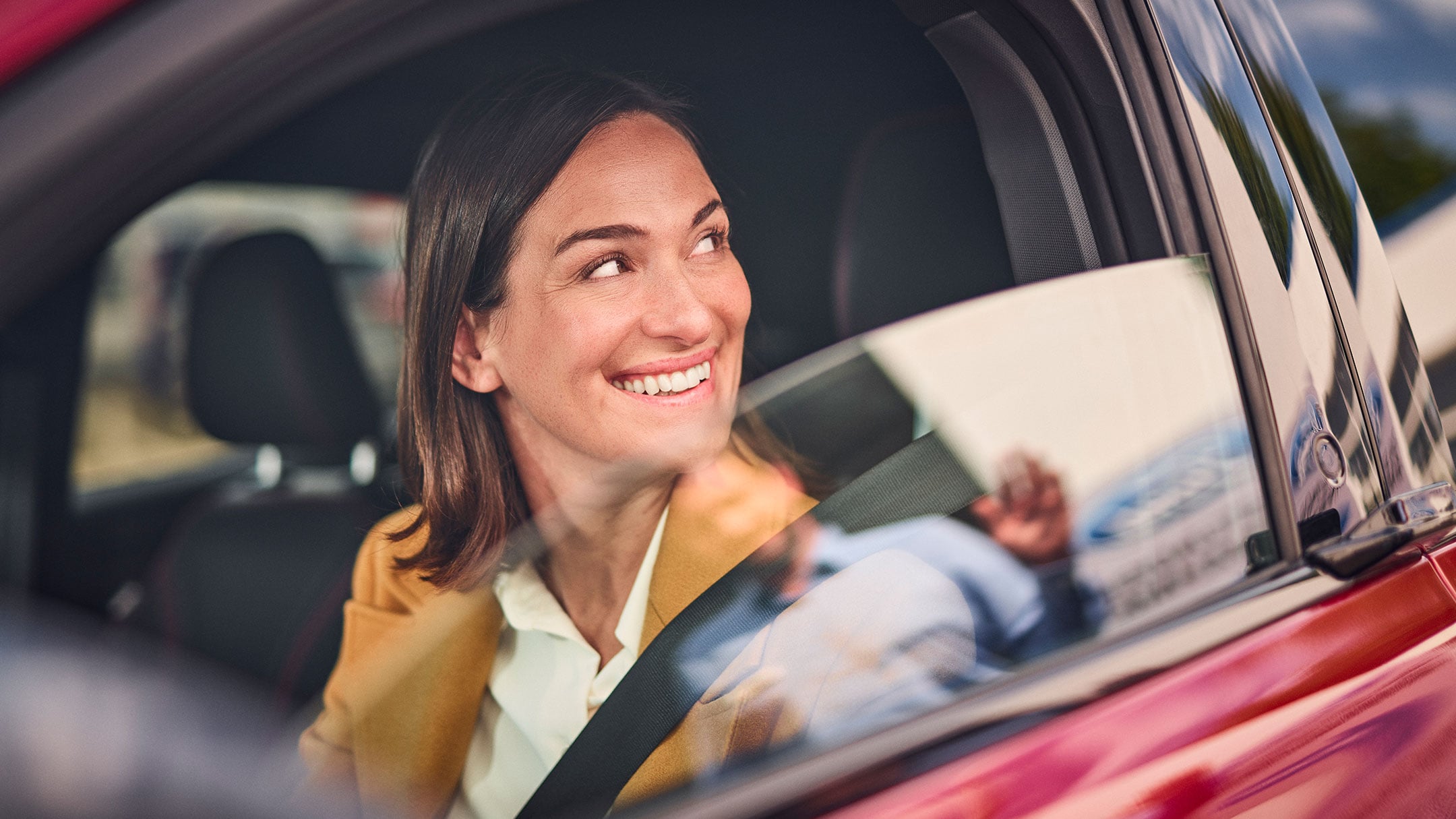 Una donna sorridente seduta a bordo di una Ford rossa.