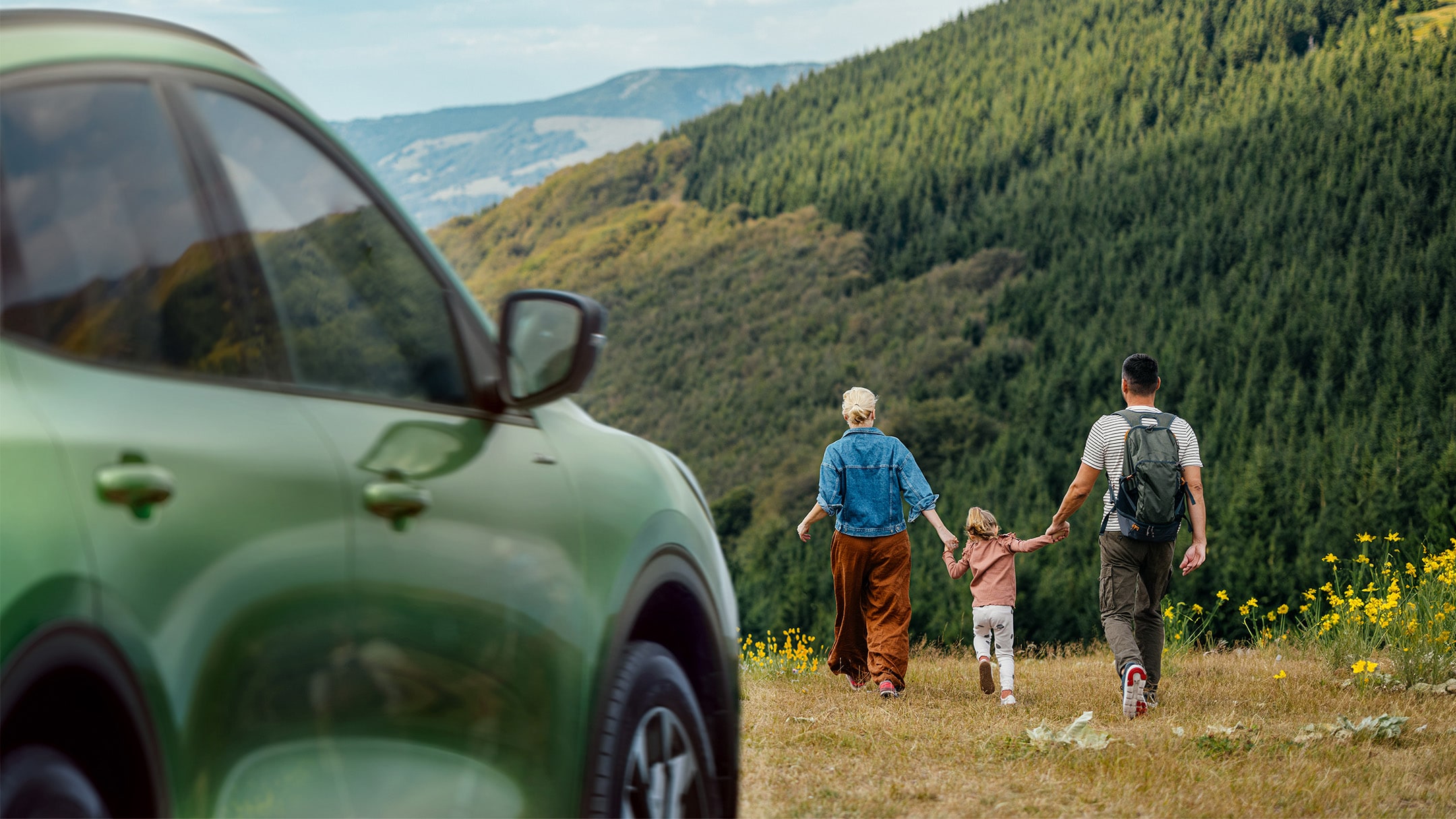 Family walking in a field by a green Ford Kuga