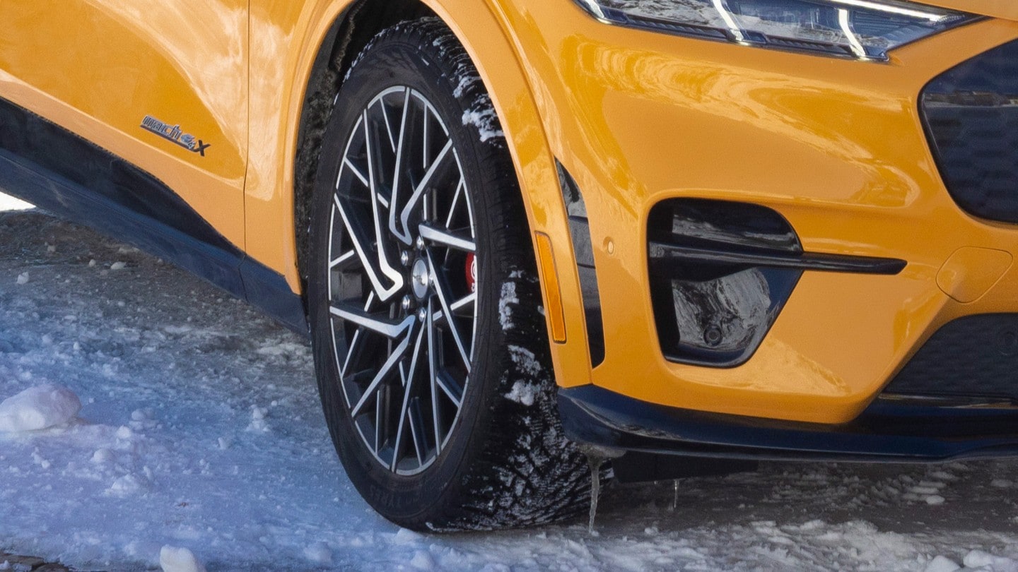 CH-DE: Nahaufnahme des Vorderrades und des Kotflügels eines leuchtend gelben Autos, wahrscheinlich ein Ford Mustang Mach-E, das auf einer schneebedeckten Fläche geparkt ist.   CH-DE: Nahaufnahme des Vorderrades und des Kotflügels eines leuchtend gelben Autos, wahrscheinlich ein Ford Mustang Mach-E, das auf einer schneebedeckten Fläche geparkt ist.